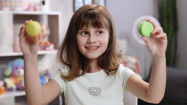 Joyeux visage souriant d'une petite fille couvrant ses yeux de macarons sur un fond de maison coloré. Dents sucrées, aliments malsains, pas de régime. Etre heureux. Portrait féminin. — Video