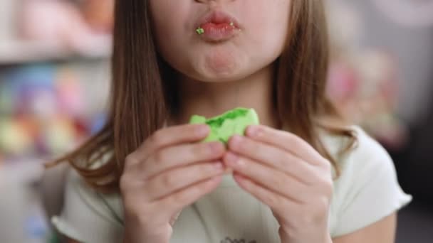 Close up de menina da escola lindo mordendo macaroon francês, gostando de comer, desejo de confeitaria e prazer. Menina feminina morena atraente no fundo da casa, lambe os lábios, comer macaron — Vídeo de Stock