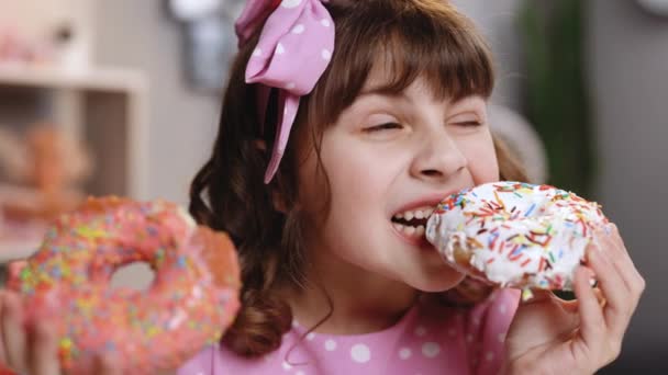 Niña caucásica comiendo sabroso donut mirando a la cámara. Niño disfrutando de donuts y comida azucarada. Concepto de comida poco saludable. Diente dulce. — Vídeo de stock