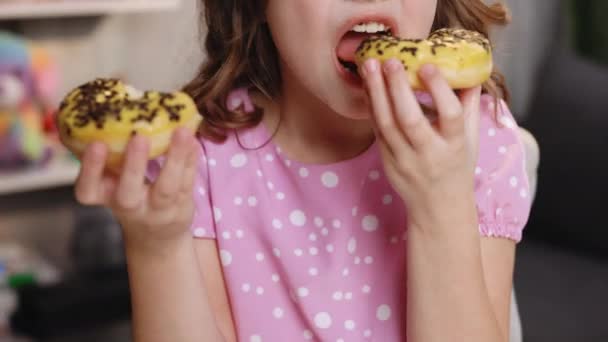 Πορτρέτο της νεαρής πεινασμένης κοπέλας τρώει ντόνατ. Το γυναικείο στόμα δαγκώνει ένα καρβέλι. Κοντινό πλάνο γυναίκα τρώει ντόνατ, νόστιμο, γλυκό, γλυκό δόντι στο σπίτι φόντο. — Αρχείο Βίντεο