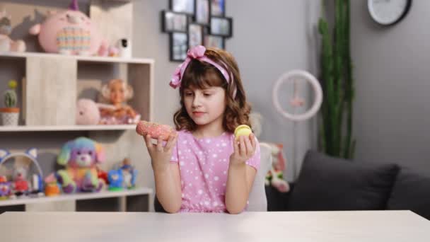 Мила радісна школярка не може вибрати між рожевим пончиком і жовтими свіжими макарунами. Здоровий спосіб життя, солодощі, солодкий зуб. Бути на дієті — стокове відео