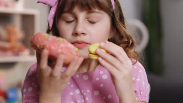 Close-up van aantrekkelijke schoolmeisje op thuis achtergrond, likt haar lippen, snuiven donut en gele macaron, sluit haar ogen met plezier. Dessert persoon, zoetekauw, fijnproever. Goed gevoel, heerlijk. — Stockvideo