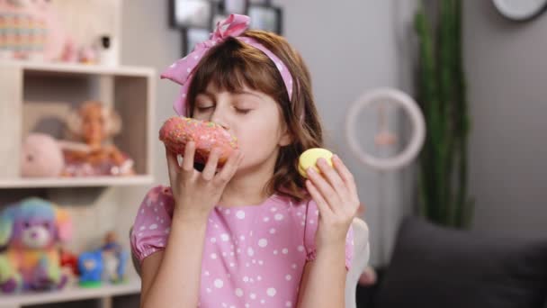 Aantrekkelijk schoolmeisje snuiven donut en gele macaron, sluit haar ogen met plezier op thuis achtergrond. Dessert persoon, zoetekauw, fijnproever. Goed gevoel, heerlijk. — Stockvideo