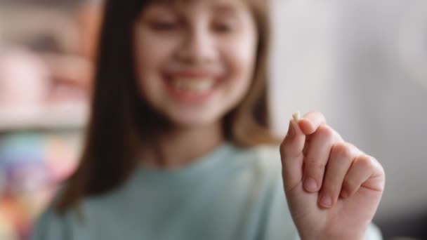 У девочек выпал молочный зуб. Довольный ребенок держит зуб в руке. Потеря молочных зубов, замена постоянных зубов. Дети это стоматология. Не показывай зубы. Удалите молочный зуб — стоковое видео
