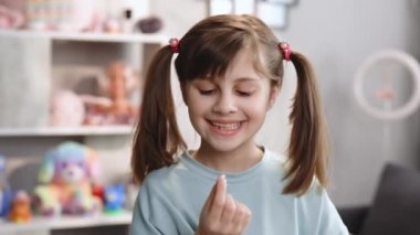 Çocukların süt dişleri döküldü. Memnun kız ağzından süt dişini çıkardı ve şaşırdı. Küçük tatlı kız süt dişini gösteriyor ve kameraya gülümsüyor yatak odasında duruyor.