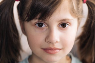 Küçük güzel bir kızın yakın plan portresi. Kafkasyalı küçük kız kameraya bakıyor. Mutlu çocukluk kavramı.