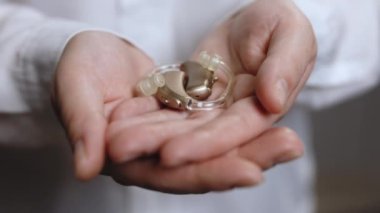 İşitme cihazı taşıyan yaşlı kadına yakın çekim. İşitme cihazı dişinin avucunda. İşitme cihazı kavramı. Beyaz arka planda işitme cihazı tutan kadın