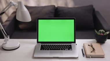Krom anahtar teknolojisi için yeşil ekranlı defter oturma odasındaki masaya yakınlaştırma görüntüsü, evdeki uzaktan çalışma yeri. Ev çalışma masasında anahtar yeşil ekran maketi olan dizüstü bilgisayar