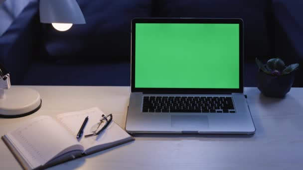 Amplie o Shot of Mock-up Green Screen Laptop em pé na mesa no escritório criativo moderno. Iluminação noturna quente e estúdio de espaço aberto com vista da janela da cidade no fundo — Vídeo de Stock