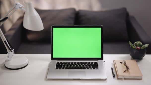 Ordenador portátil de pantalla verde en el escritorio del hogar junto a una lámpara de escritorio. Portátil con pantalla verde en blanco. Interior del hogar o loft fondo de oficina — Vídeo de stock
