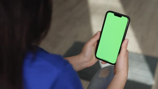 Zadní pohled brunetky dívka drží chroma klíč zelená obrazovka makat do smartphone sledování obsahu, aniž by se dotkl nebo přejel. Použít zelenou obrazovku pro kopírování prostoru. Gadgets a moderní lidé koncept — Stock video