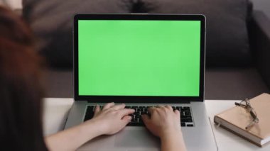 Laptopta yeşil ekranlı, tahta masada oturan bir kadının arka görüntüsü. Bilgisayarda masasında çalışan bir kadın, kromakey. Kadın yeşil maket ekranlı dizüstü bilgisayar kullanıyor.