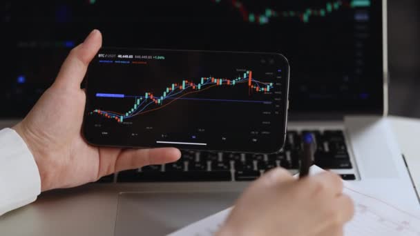 Trader mercato azionario analizzando andamento dei prezzi bitcoin. Grafico dei dati dell'analisi del mercato azionario dei broker di investimento con i tassi di prezzo. Trading valuta Bitcoin crypto utilizzando laptop e smartphone. — Video Stock