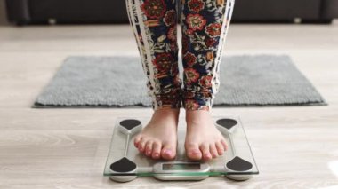 Closeup of barefoot woman using digital scales and checking her weight. Female feet step on floor scales. Concept of dieting, loosing weight and healthy lifestyle