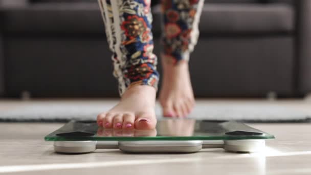 Walking kvinna kontrollerar BMI viktminskning. Flicka barfota mäta kroppsfett övervikt. Kvinnan på våg mäter vikten. Flickben kliver på badrumsskalan. Föda kvinna fötter stående våg på rummet — Stockvideo