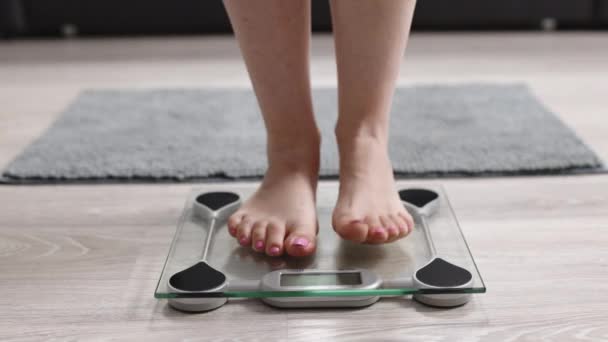 소녀는 화장실 저울 위로 발을 내딛는다. 여성은 체중을 측정 할 수있는 척도 가 있다. 사람 의발은 체중 과 다 지방을 측정 한다. 체중줄이기 BMI 체중 감소를 확인하는 슬림 여성. 체중 이 줄어 방에 앉아 있는 다이어트 여성 의발. — 비디오