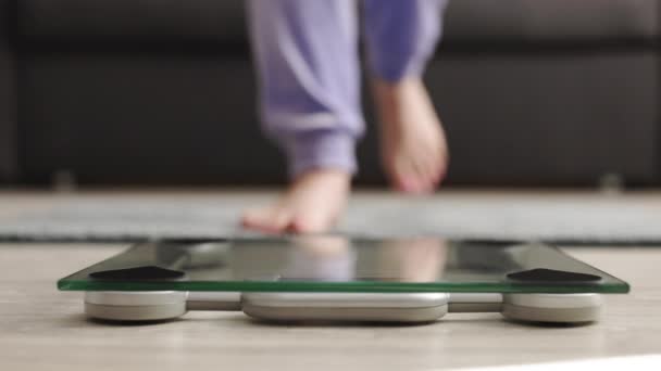 Samice měřící váhu zblízka na stupnici zdravotního stavu. Ženské nohy se blíží k vážení digitálního přístroje. Ženy nohy, demonstrující vážení-out proces izolované na domácím pozadí. — Stock video