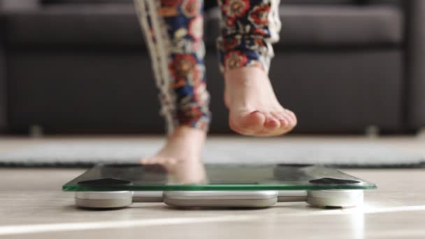 Person checking the weight on the scale. Close-up portrait of womans legs, demonstrating weigh-out process isolated on home background — Stok Video