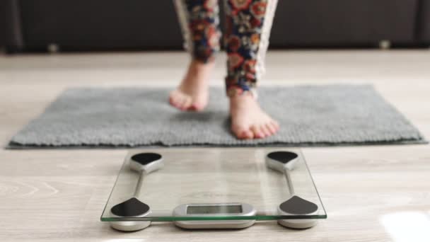 체중을 재기 위해 저울 위에 서 있는 소녀의 다리. 백인 여성의 맨발로 집에서 몸무게를 재고 있습니다. 몸무게를 재는 사람도 있다. 다이어트, 조정 및 측정. — 비디오