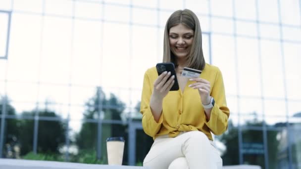 Leende Flicka Med Kreditkort Och Smartphone Sitter Bänk Stadsbyggnader Utomhus — Stockvideo