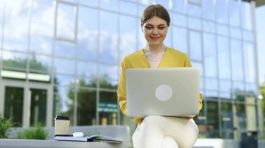 Modern ofisin yanındaki dizüstü bilgisayarda çalışan kablosuz kulaklık kullanan odaklanmış bir iş kadını. Dizüstü bilgisayar klavyesinde yazan kadın yönetici. Laptop ekranına bakan gülümseyen iş kadını portresi.