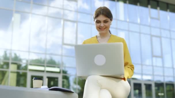 在办公室外看着笔记本电脑的高加索女商人 一个微笑的女孩在户外的笔记本边喝咖啡 快乐的女商人在遥远的工作场所对着手提电脑摄像机微笑 — 图库视频影像