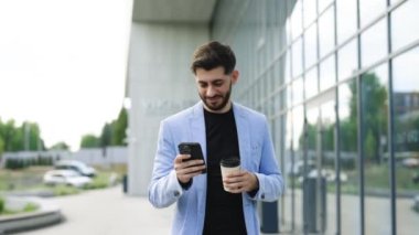 Mutlu Ermeni genç sakallı girişimci cep telefonu interneti tarıyor ofis molasında kahve içiyor iş yeri boyunca yürüyor. Başarılı bir iş adamı işe gidiyor..