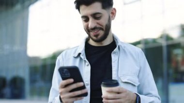 Akıllı telefon mesajlarında sosyal medya uygulaması kullanarak genç ve zarif sakallı bir adama dışarıda gülümseyen haberler gönderiliyor. İnsan portreleri. Teknoloji.