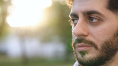 Çekici esmer, sakallı, yakışıklı bir adam gün batımında kahverengi gözlerin etrafında gülümsüyor. Dışarıda dur ve rahatla. Mutlu rahatlama. Kapatın. Yavaş çekim 100fps