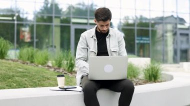 Gülümseyen sakallı iş adamı modern ofisin yanındaki dizüstü bilgisayarda çalışıyor. İş yerinde dizüstü bilgisayarda daktilo kullanan profesyonel bir erkek. Dışarıdaki dizüstü bilgisayara bakan pozitif iş adamının portresi