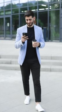 Muhteşem sakallı iş adamının finans bölgesinde cep telefonu kullanarak mesaj attığı dikey format videosu, cep telefonu mesajlaşması sırasında başarılı erkek CEO 'nun gülümsemesi.