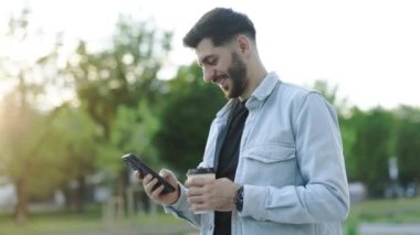 Yakışıklı beyaz Ermeni genç adam gün ışığında sokakta telefon kulübesi kullanıyor. Mobil teknoloji. Modern moda iş adamı hücresi. Portre. Açık hava..