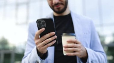 Kendine güvenen Ermeni işadamı modern şehir bölgesinde elinde kahve fincanı tutan cep telefonu kullanıyor. Pozitif iş adamı açık havada gülümseyen finans haberlerine bakıyor. Başarılı bir yetişkin adam..