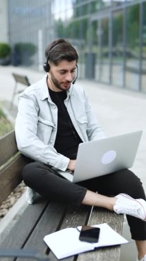 Adamın dikey videosu kulaklık takıyor ve online öğretmenle laptopta konuşuyor. Bilgisayar kameralı sohbet kullanarak öğrenen erkek öğrenci notlar alır. Uzaklık eğitimi kavramı