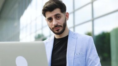 Laptop 'ta çalışan, borsa verilerini kontrol eden, kameraya bakıp gülümseyen genç, sakallı beyaz adam portresi. Mutlu, neşeli, başarılı, gülümseyen bir komisyoncu. İşadamı.