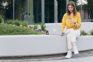 Çevrimiçi dükkanda hızlı ve kolay ödemeler yapan bir bayan müşteri. E-bankacılık uygulama servisi. Elinde kredi kartı ve akıllı telefon olan bir kız şehir merkezindeki bankta oturuyor..