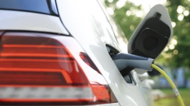 Elektrikli araç yükleme portu. Kadın elleri elektrikli otomobilinin fişini çekiyor. Elektrikli araba şarj aletinin fişini çeken bir kadın. Kapağın altından, elektrikli eko arabanın 4K UHD şarj ettiği bir çekim.