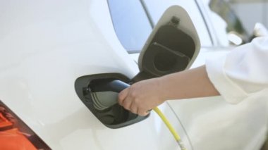 Womans hands unplugging her electric automobile and closing the hatch in front of her home. Female unplugging the power supply cable from an white electric car.