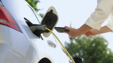 Modern elektrikli arabayı şarj etmek için akıllı telefon kullanarak kadın ellerini kapat. Kadın elleri elektrikli otomobilinin fişini çekiyor ve şarj istasyonunun kapağını kapatıyor..