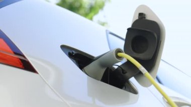 Kadın elleri elektrikli otomobilinin fişini çekiyor ve evinin önündeki kapağı kapatıyor. Kapağın altından, elektrikli çevreci arabanın şarj olduğu yerden. Elektrikli araç şarj portu.