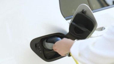 Kadın, çevre dostu elektrikli arabasını evde şarj ediyor. Bir kadının ellerinin, şarj etmek için elektrikli arabasını fişe taktığı yakın çekim..