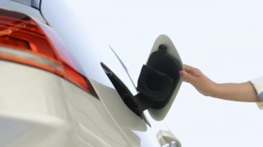 Kafkasyalı kadınların elektrikli bir arabayı açarken, soket kapağını açarken ve şarj aletini takarken yakın plan çekimleri. Kadın temiz arka planda modern sıfır emisyon araba şarj.
