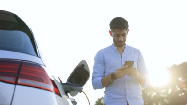 Biały Mężczyzna Brodą Używający Smartfona Czekający Podłączenie Zasilania Pojazdów Elektrycznych — Wideo stockowe