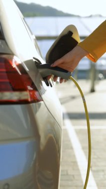 Elektrikli araba kablosunu söken bayanın dikey format videosu. Kadın elleri elektrik kablosunu koparıp elektrikli arabayı şarj ediyor. Çevre dostu alternatif enerji yeşil çevre kavramı