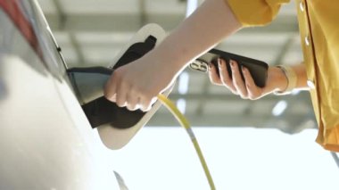 Elektrikli araba kablosunun fişini çeken kadın. Kız cep telefonu akıllı telefonunda uygulamayla şarj olmayı kesti. Çevre dostu nakliye aracı. Kadın eli elektrik kablosunu koparıp elektrikli arabayı şarj eder..