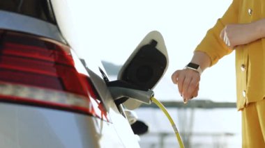 Tanımlanamayan bir kadın elektrikli araba kablosunun fişini çekiyor. Kız, takılabilir akıllı saat için uygulama kullanmaktan vazgeçti. Kadın eli güç kablosunu koparıyor. Çevre dostu alternatif enerji taşımacılığı.