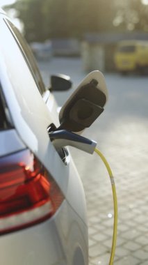 Vertical video of unrecognizable man plugging in charging cable to to electric vehicle. Male hand inserts power connector into EV car and charges batteries uses smartwatch for activates start charging