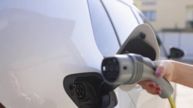 Close up of woman hand holding electric car cable for recharge plug in hybrid electric vehicle at home or charging station. World Environment Day. Save world save life concept.