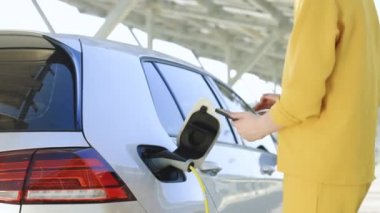 Kız cep telefonu akıllı telefonunda uygulamayla şarj olmayı kesti. Çevre dostu nakliye aracı. Kadın eli elektrik kablosunu koparıp elektrikli arabayı şarj eder. Elektrikli araba kablosunu söken kadın.
