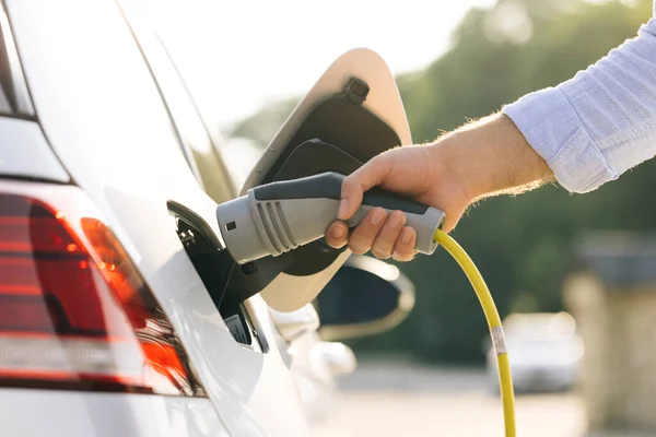 Elektrikli arabaya elektrik kablosu bağlayan tanınmayan bir adam. Elektrikli araç şarj ediliyor. Pili şarj ediliyor. Modern EV fişi takılı. Ekoloji alternatif enerjisini gelecek sürdürülebilir olarak kaydet.